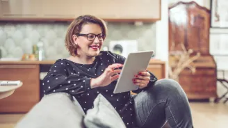 A Woman Smiles as She Looks at Content of Her Tablet at Home.