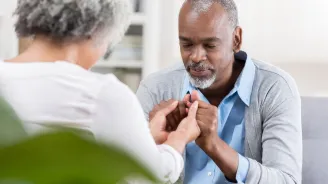 Elderly couple sitting across from each other, clasping hands, and praying together.