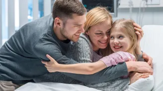 A family hugging their young daughter in her hospital bed.