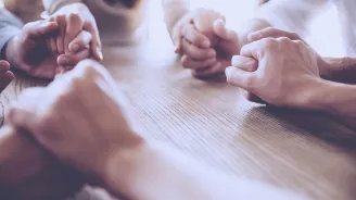 A group of friends holds hands in prayer.