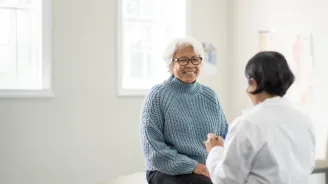 An older female patient talking to a female physician in an exam room.