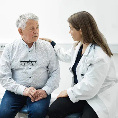 A Doctor Speaks Comfortingly With Her Senior Patient in an Exam Room 