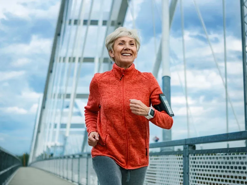 A Senior Woman Jogs Across a Bridge While Listening to Music