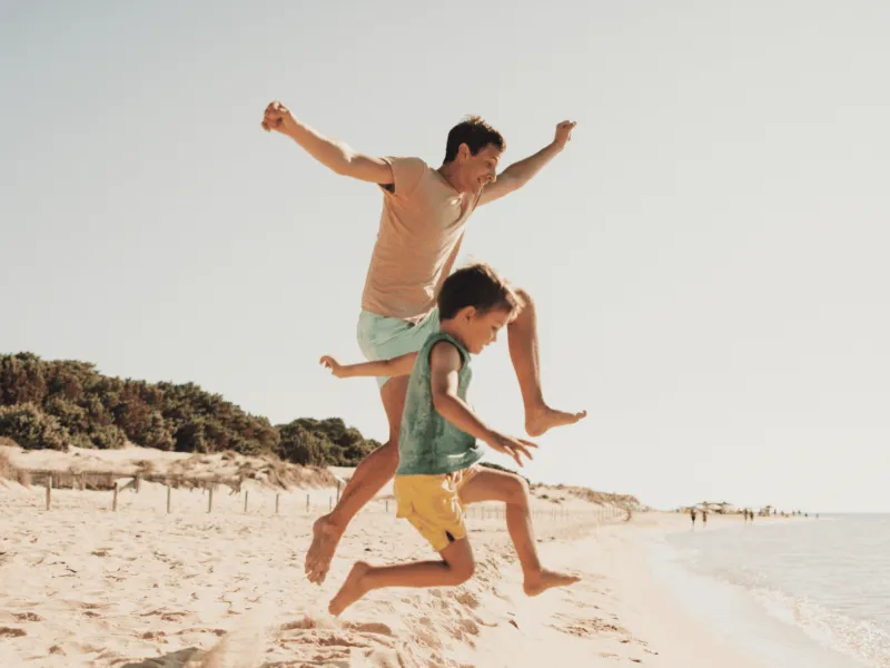 A Father and Son Jump Off a Dune on the Beach