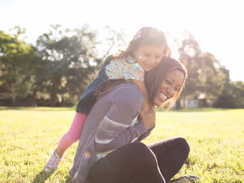 Daughter climbing on mom outdoors