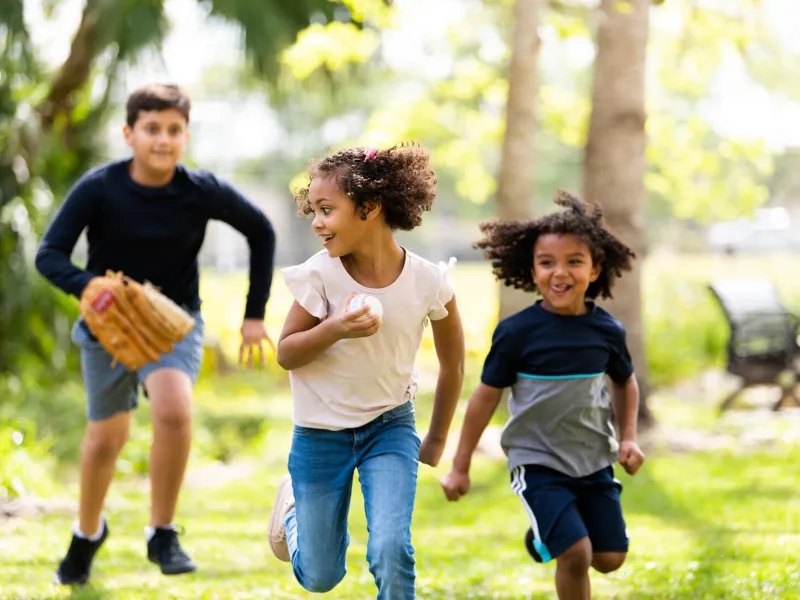 Three Hispanic Children Play Baseball in a Park