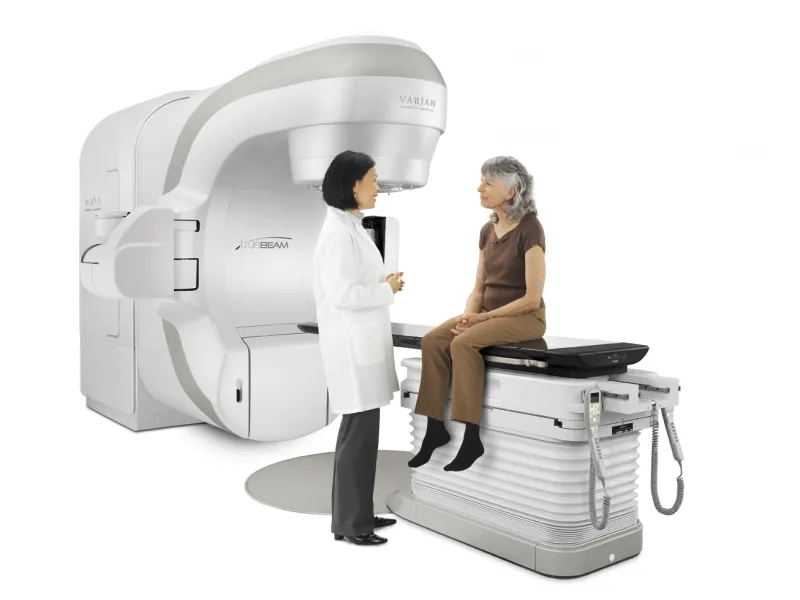 Oncologist with a female patient sitting on the bed of the TrueBeam Radiotherapy System from Varian Medical Systems.