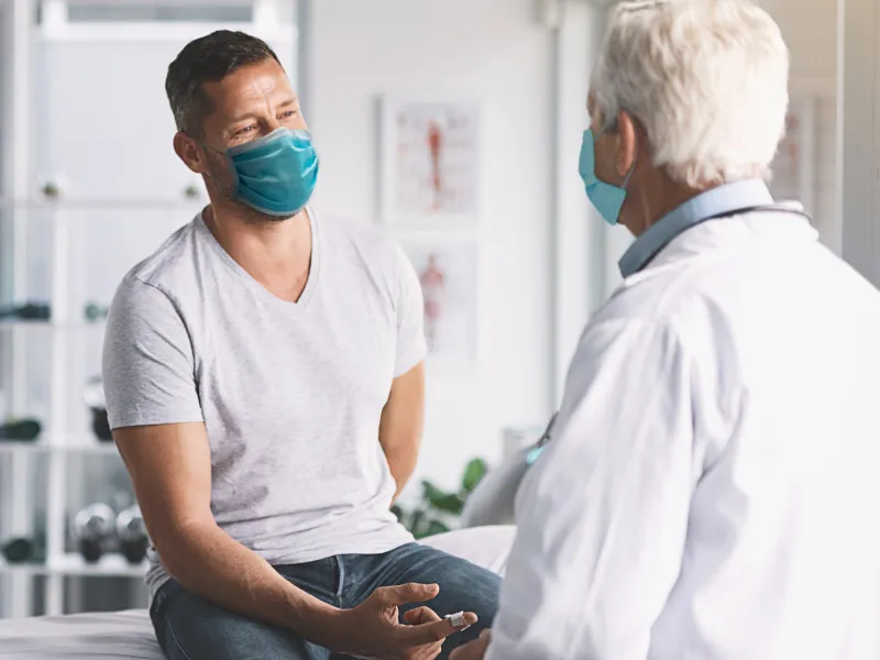Man talking with doctor while both are wearing masks.
