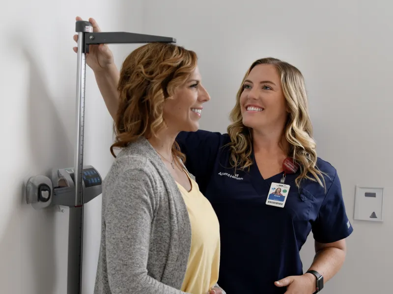A Primary Care+ Nurse Measures the Height of a Smiling Patient