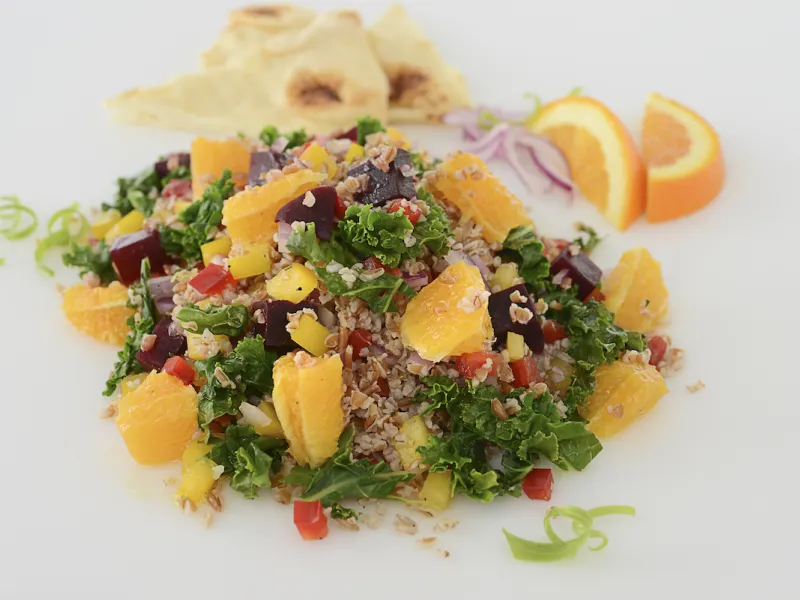 Mound of roasted beet, kale, and pepper salad with orange garnishes