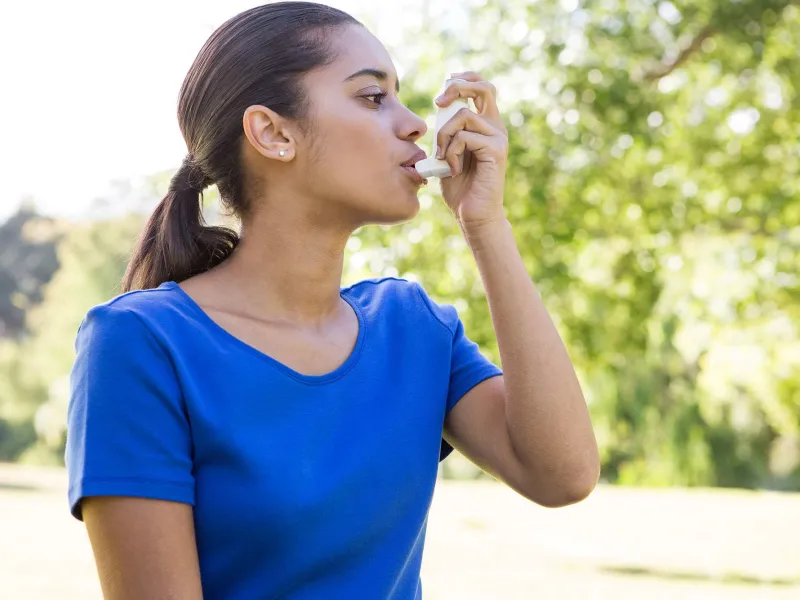 Young mixed-race woman using an asthma inhaler
