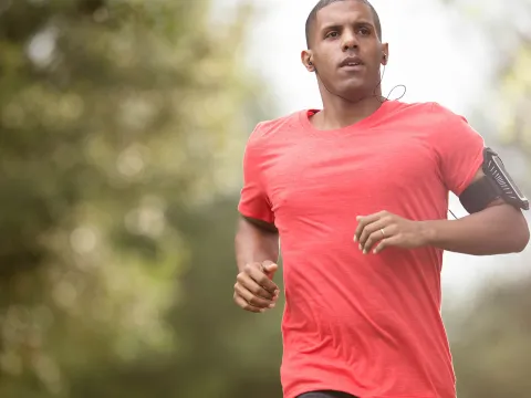 Man in a red shirt running outside while listening to music.