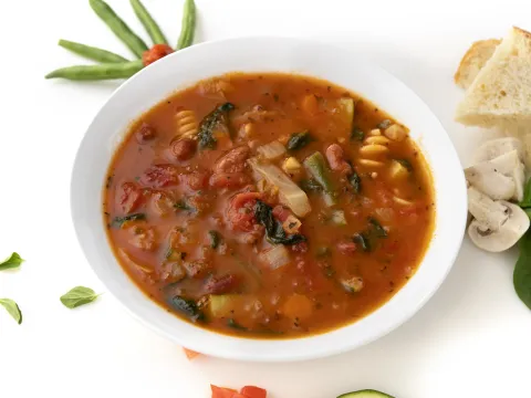 Bowl of minestrone soup with greens and mushroom garnishes
