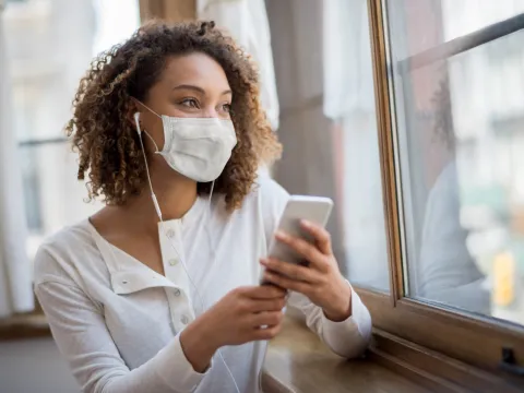 A woman wearing face mask and using her cell phone.