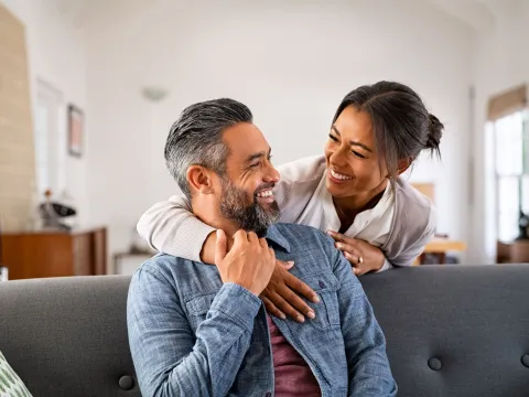 A man and woman laugh together in their living room. 