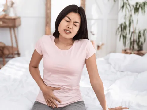 Woman sitting and holding lower abdomen in pain.