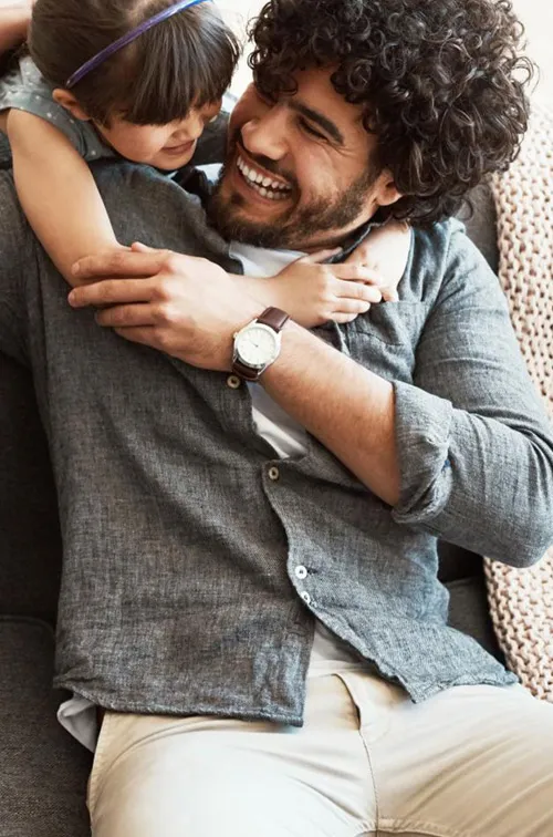 A daugther hugging her father who is sitting in the couch.